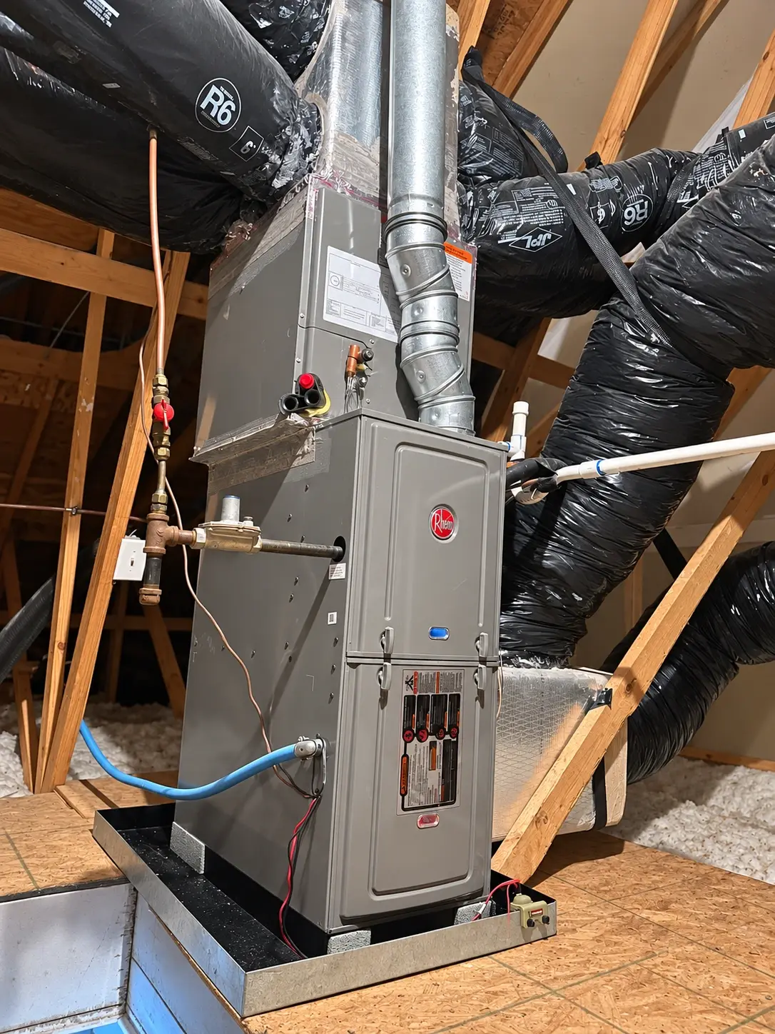 A new Rheem gas furnace installed in an attic on a drain pan, with new venting and gas line
