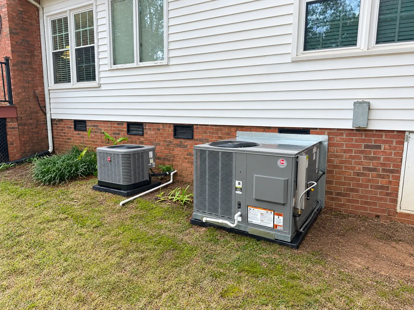 A Rheem condenser and a packaged unit installed beside a home with a crawlspace