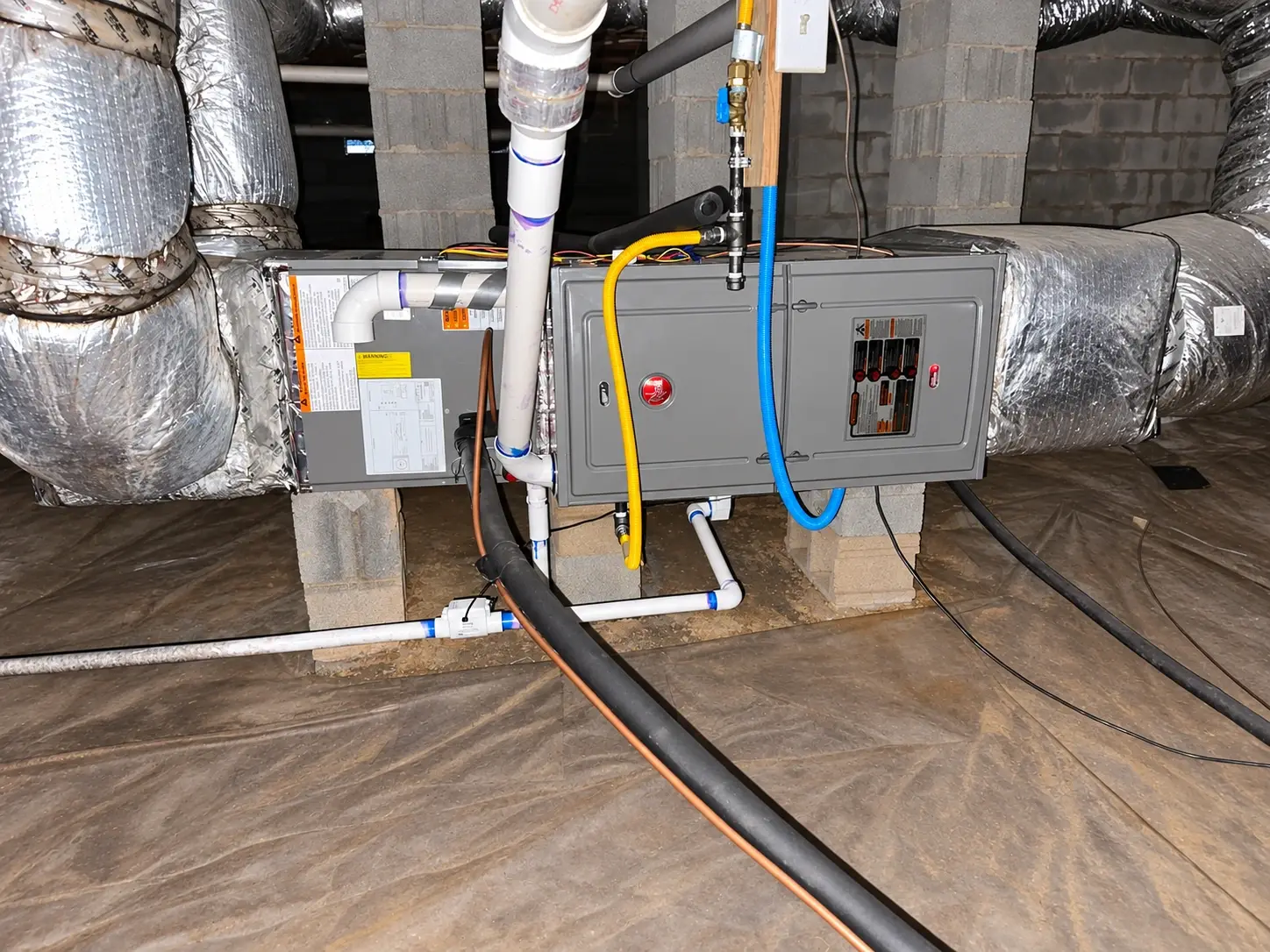 A horizontal Rheem furnace installed in a crawlspace on block supports, with insulated ductwork
