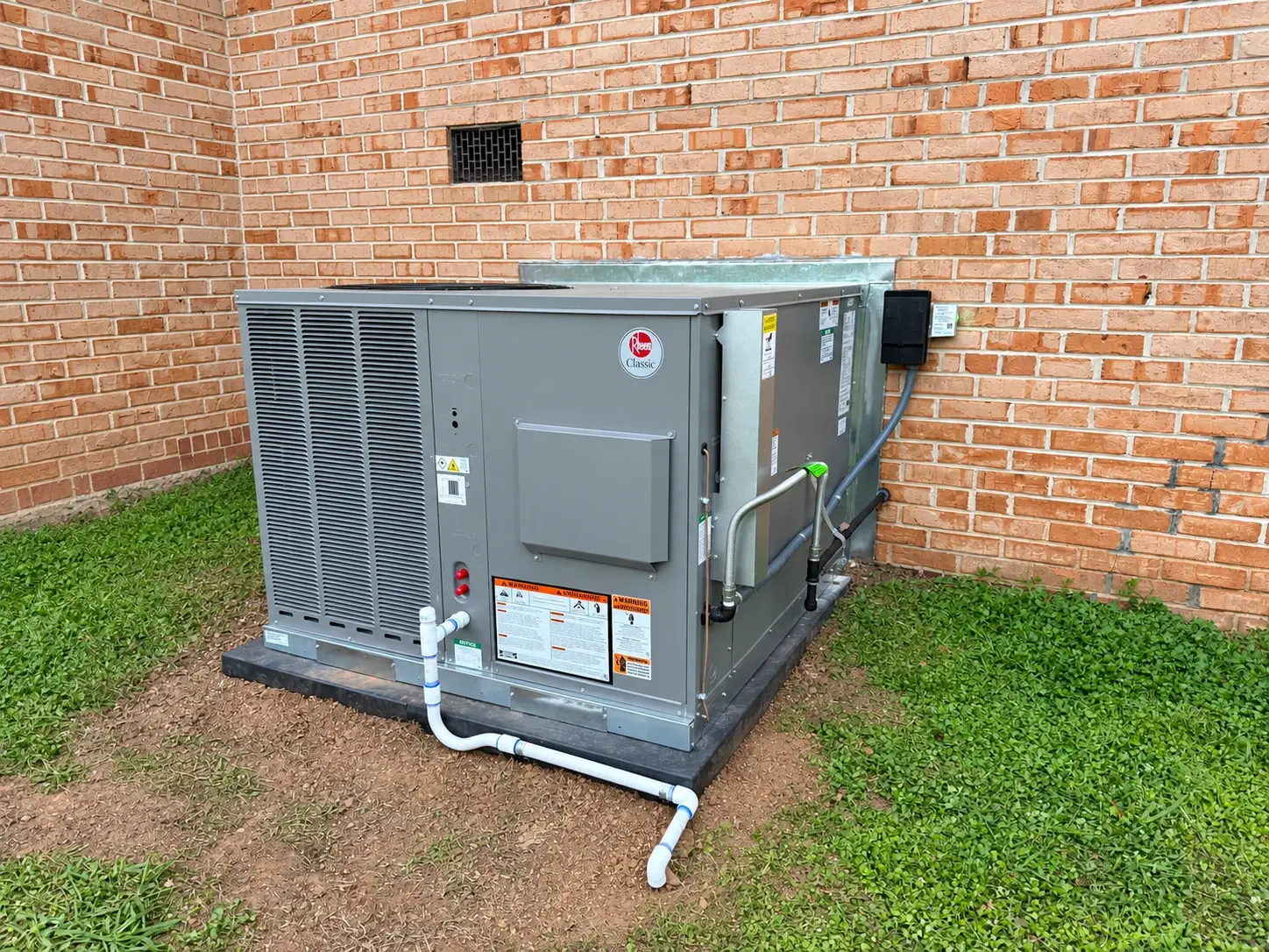 A new Rheem packaged HVAC unit on a pad beside a brick home
